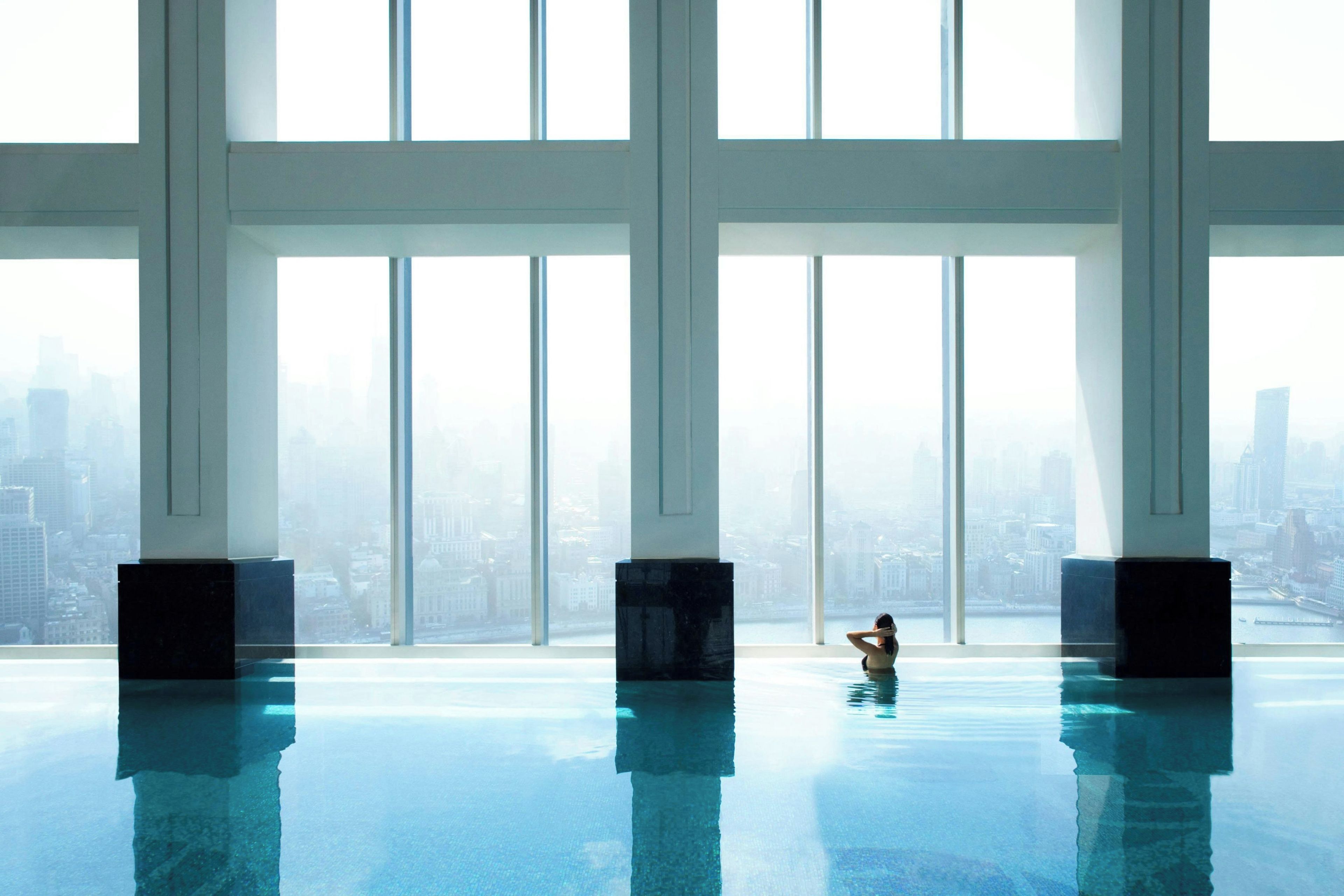 A large indoor swimming pool with a city view, high ceilings, and minimalistic design.