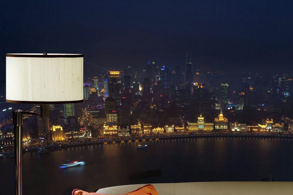 A room with a view of a city skyline at night, a lamp, and a cushion with a floral pattern.