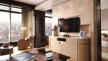Una habitación de hotel moderna con un ventanal grande, un televisor de pantalla plana, una cafetera, un sofá, una mesa de comedor y una estantería.