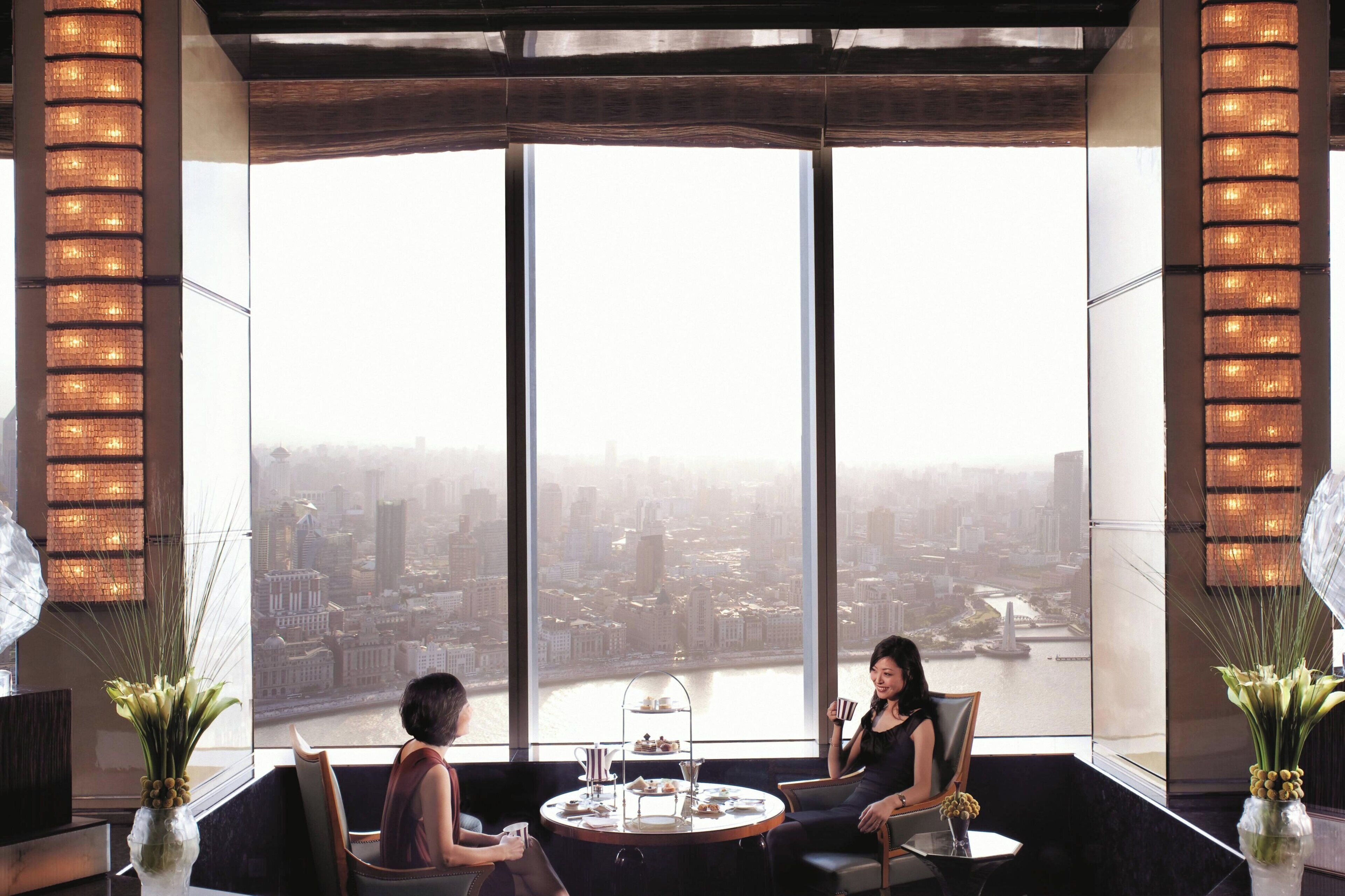 Habitación en un rascacielos con vistas panorámicas de la ciudad, una mesa redonda con servicio de té y dos sillas.