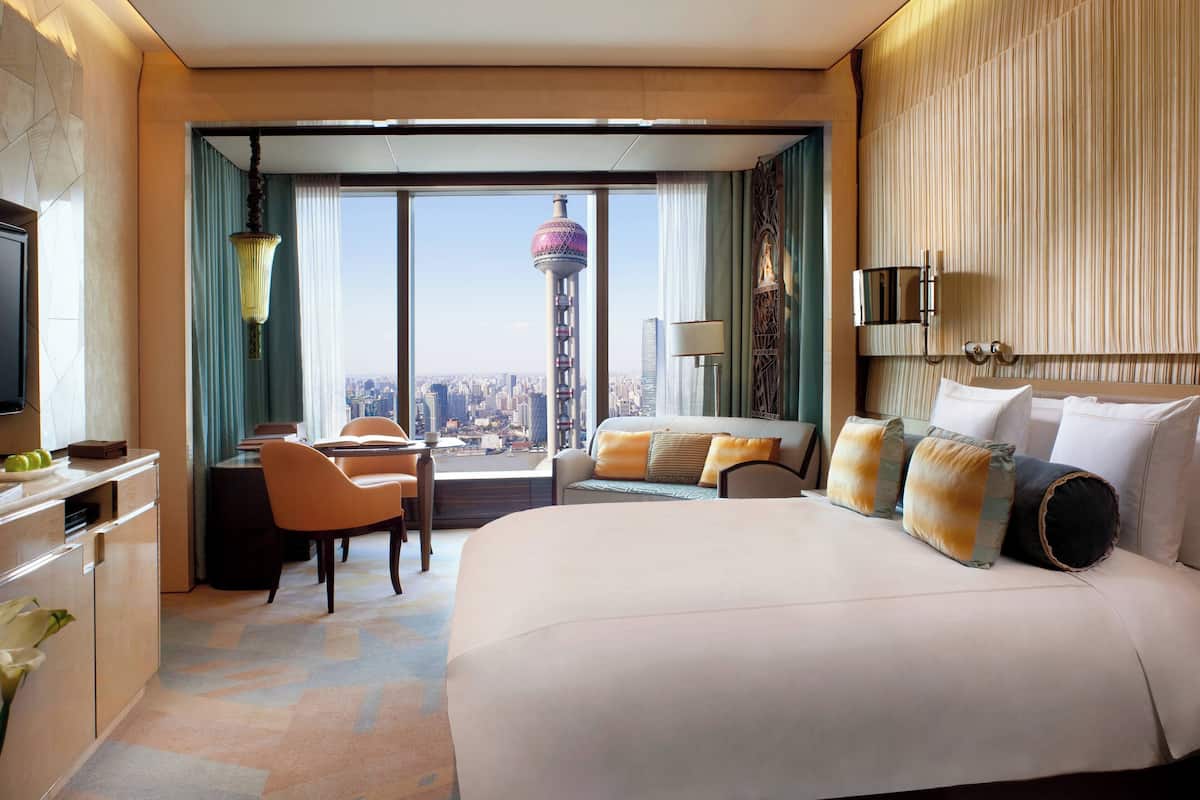 A hotel room with a large bed, a desk, and a chair. There is a view of a tower through the window.