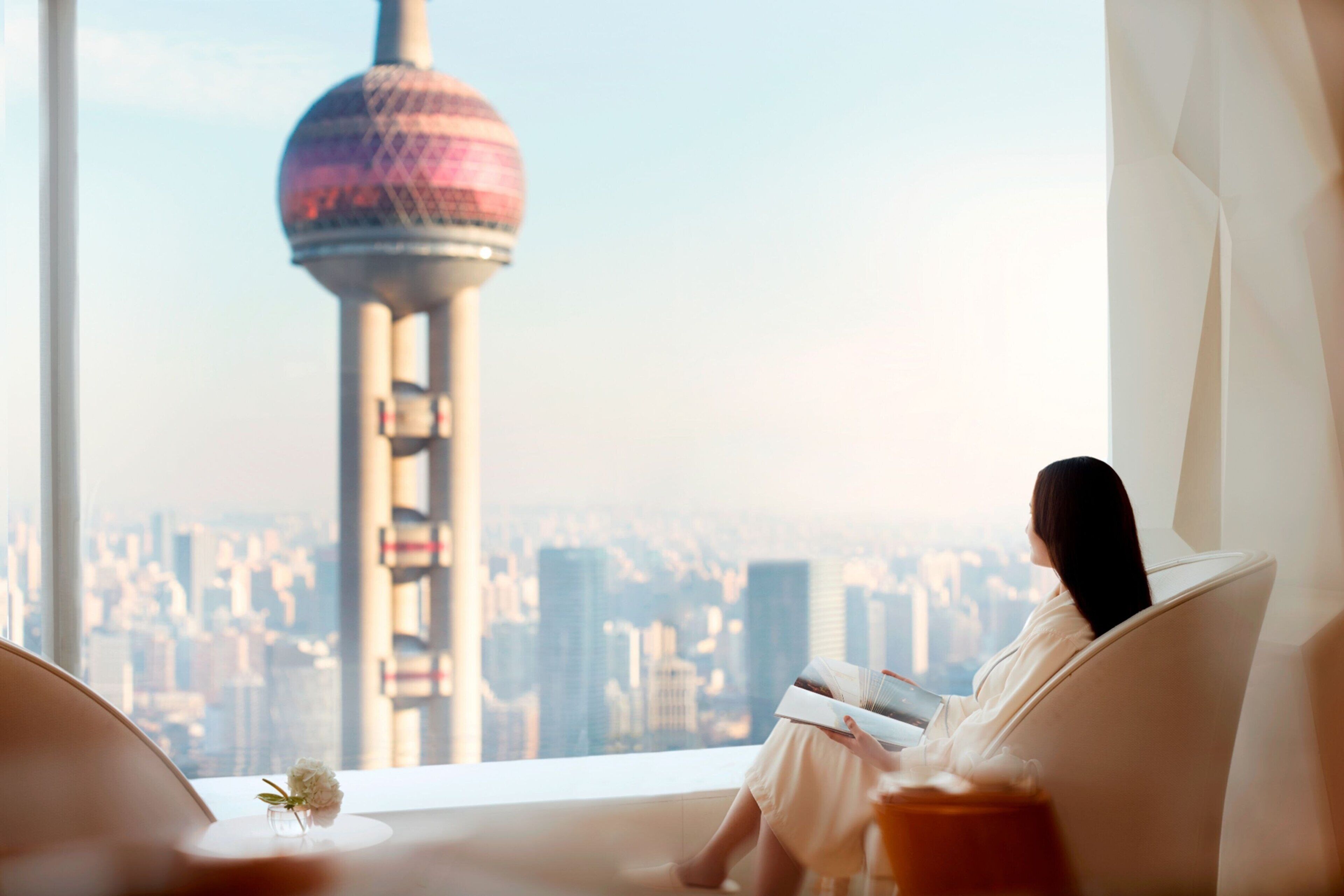 Una persona leyendo un libro en una habitación con vista a un paisaje urbano y una torre.
