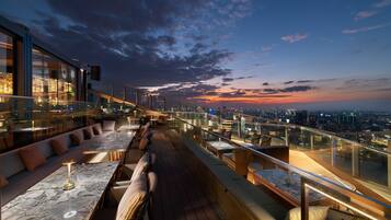 A rooftop bar with seating and a city view at sunset.
