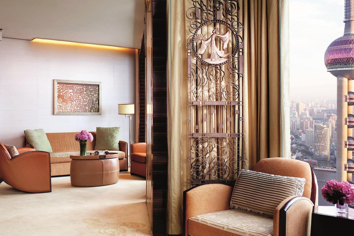 A modern living room with a sofa, armchairs, and a coffee table. There is a decorative wall panel and a view of the cityscape through the window.