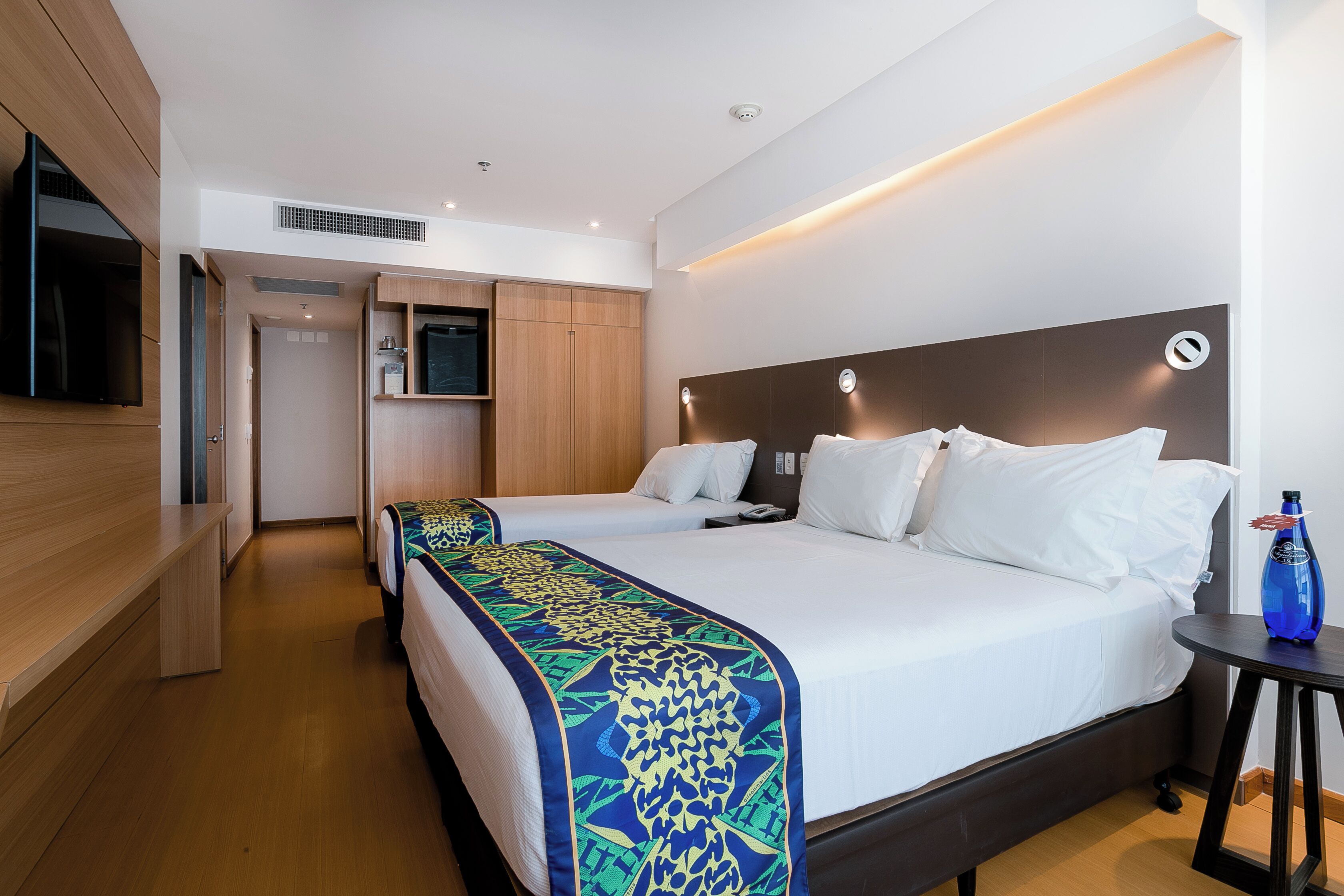 Una habitación de hotel con una cama, mesita de noche y televisor.