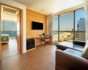 A modern hotel room with a balcony, a flat-screen TV, a desk with a chair, and a sofa.