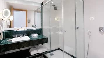 Un baño moderno con ducha envuelta en vidrio, lavamanos de mármol y espejo con iluminación.