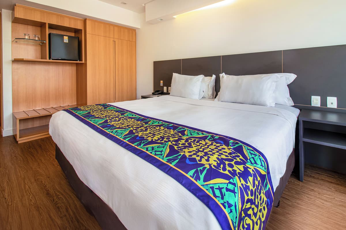 A hotel room with a large bed, a wooden wardrobe, a bedside table, and a flat-screen TV.