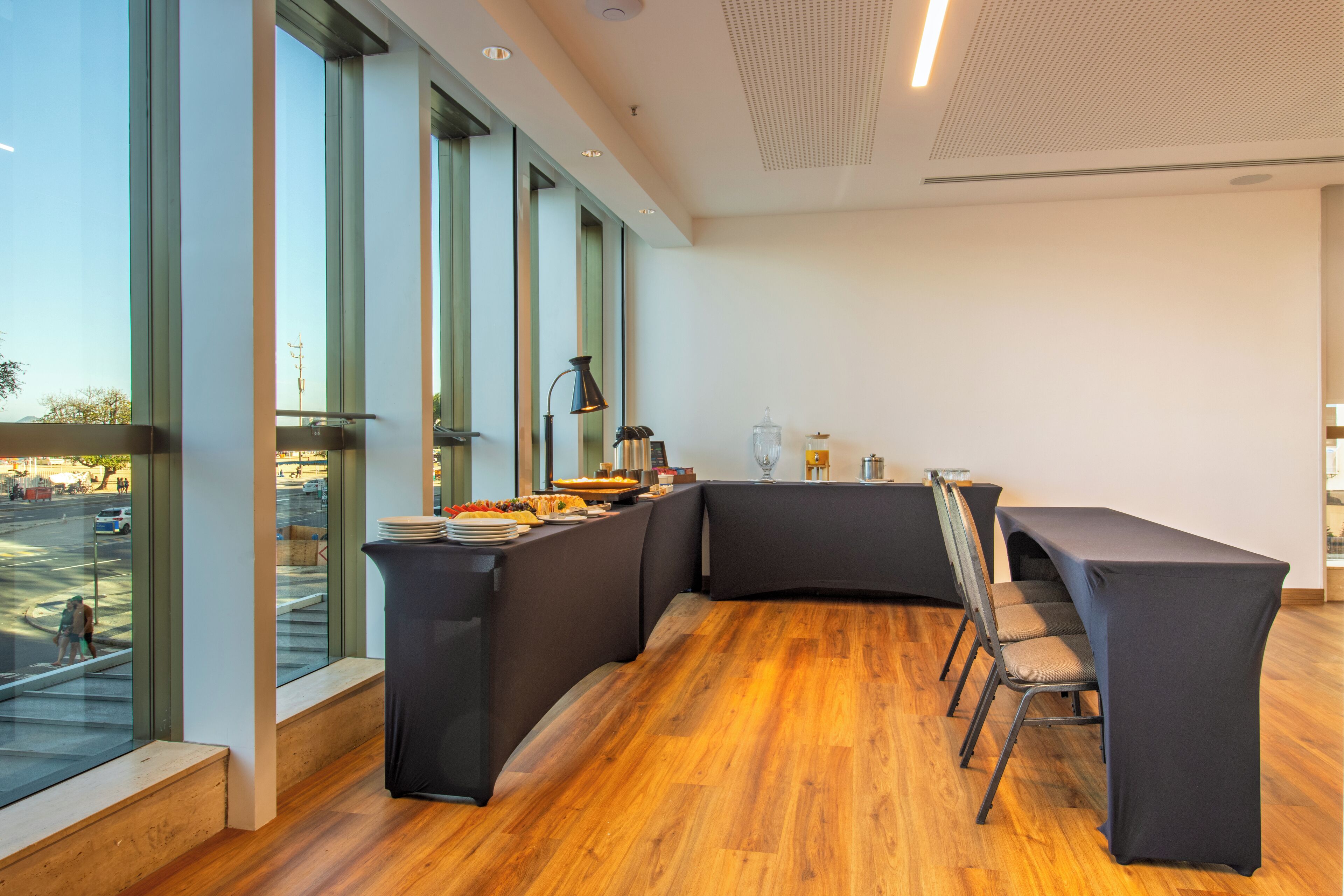 A modern dining area with a curved black table and chairs, large windows, and a view of the street.