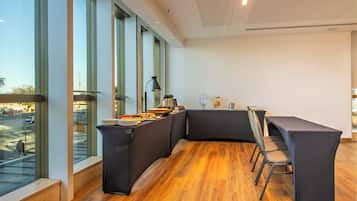 A modern dining area with a curved black table and chairs, large windows, and a view of the street.