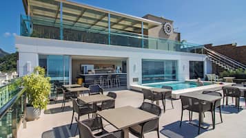 Um bar no terraço com área externa, piscina e guarda-corpo de vidro.