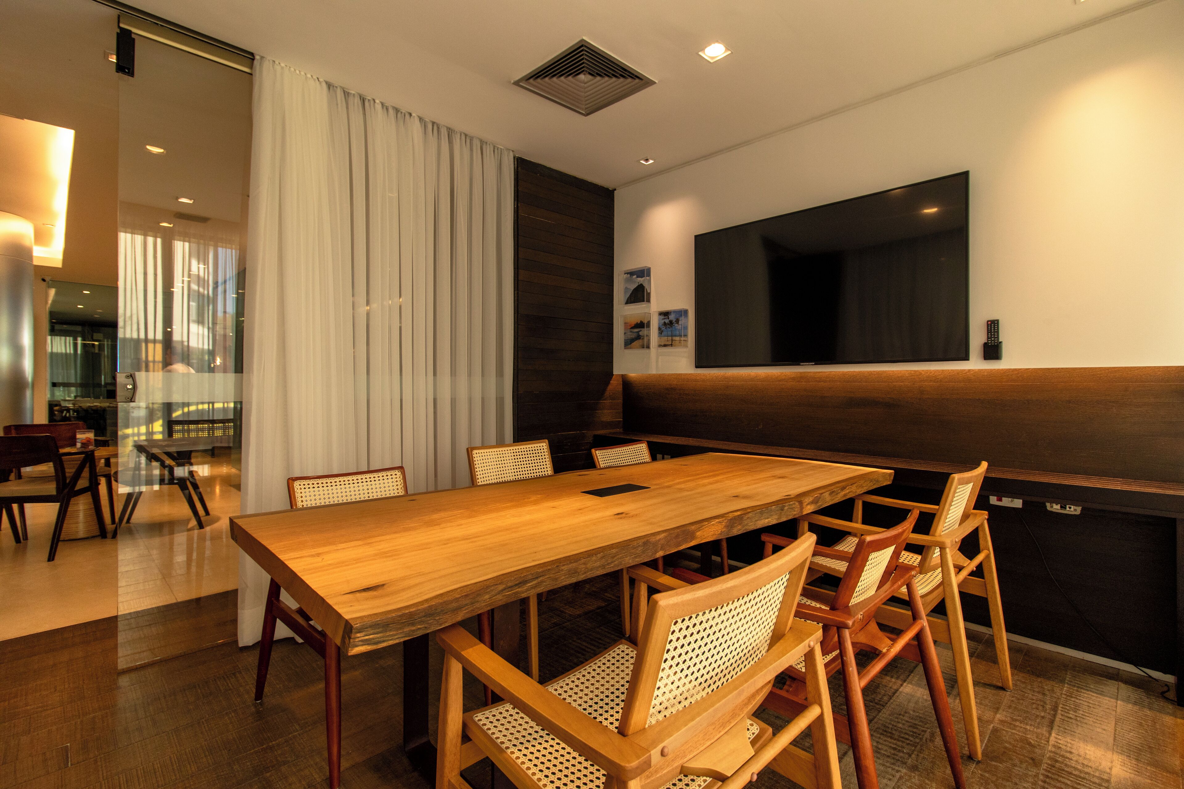 A modern dining area with a wooden table and wicker chairs, a large window with curtains, and a dark wooden accent wall.