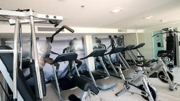 A gym with multiple treadmills, a rowing machine, and a wall with fitness posters.