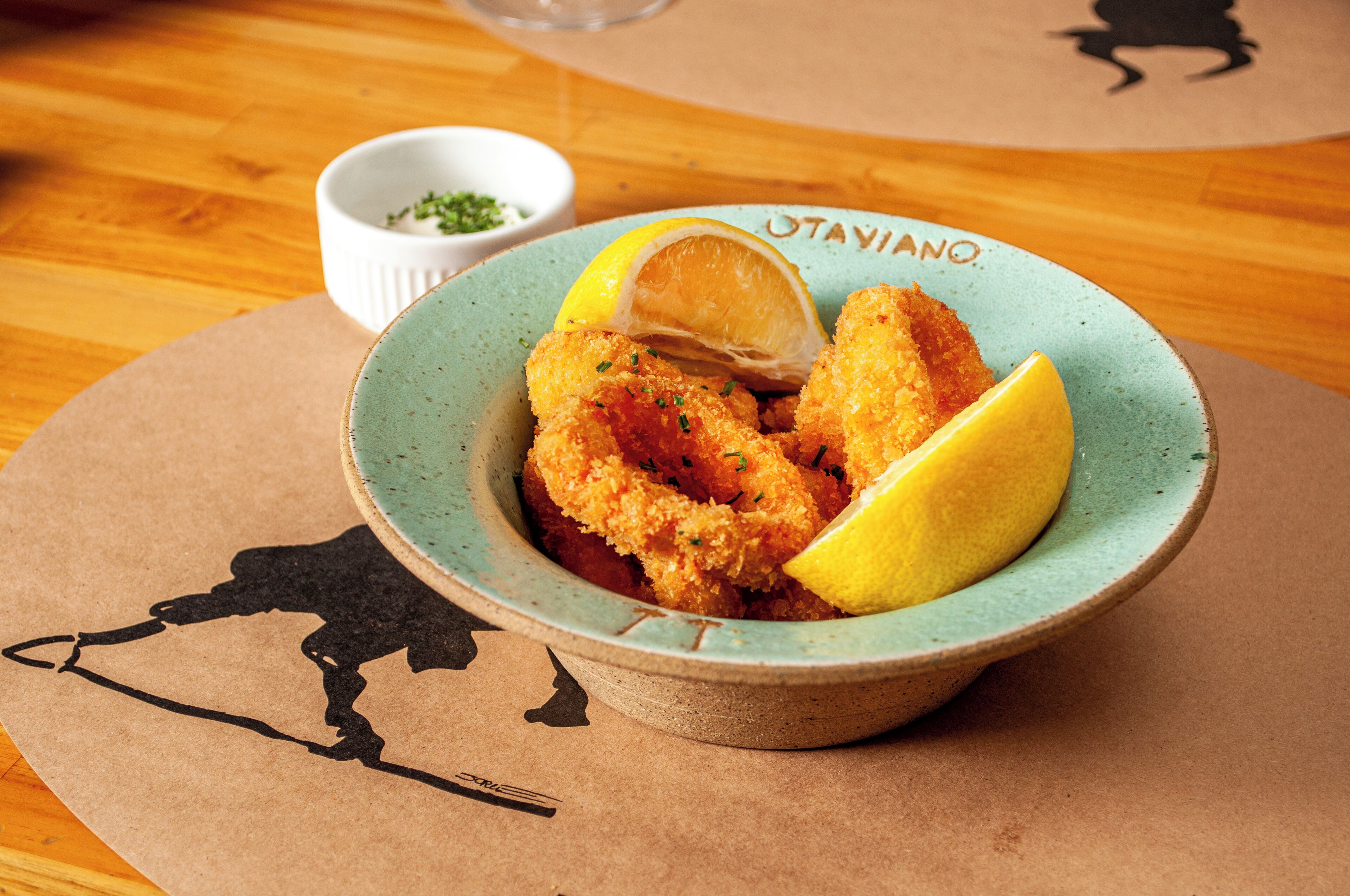 A bowl of breaded and fried food with lemon wedges on a table.
