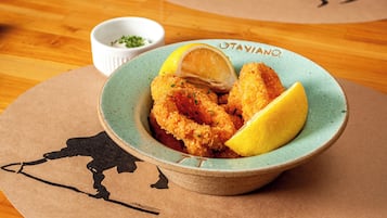 A bowl of breaded and fried food with lemon wedges on a table.