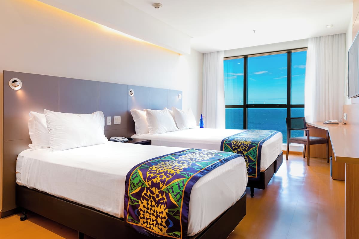 A hotel room with two beds, a desk, and a large window with a view.
