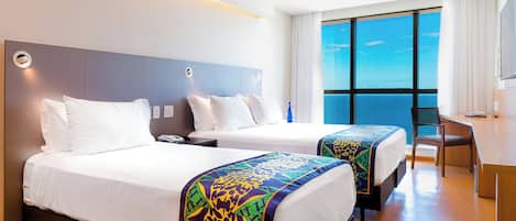 Una habitación de hotel con dos camas, un escritorio y un ventanal con vistas.