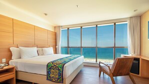 Ein Hotelzimmer mit einem großen Bett, einem Schreibtisch und Blick auf den Ozean.