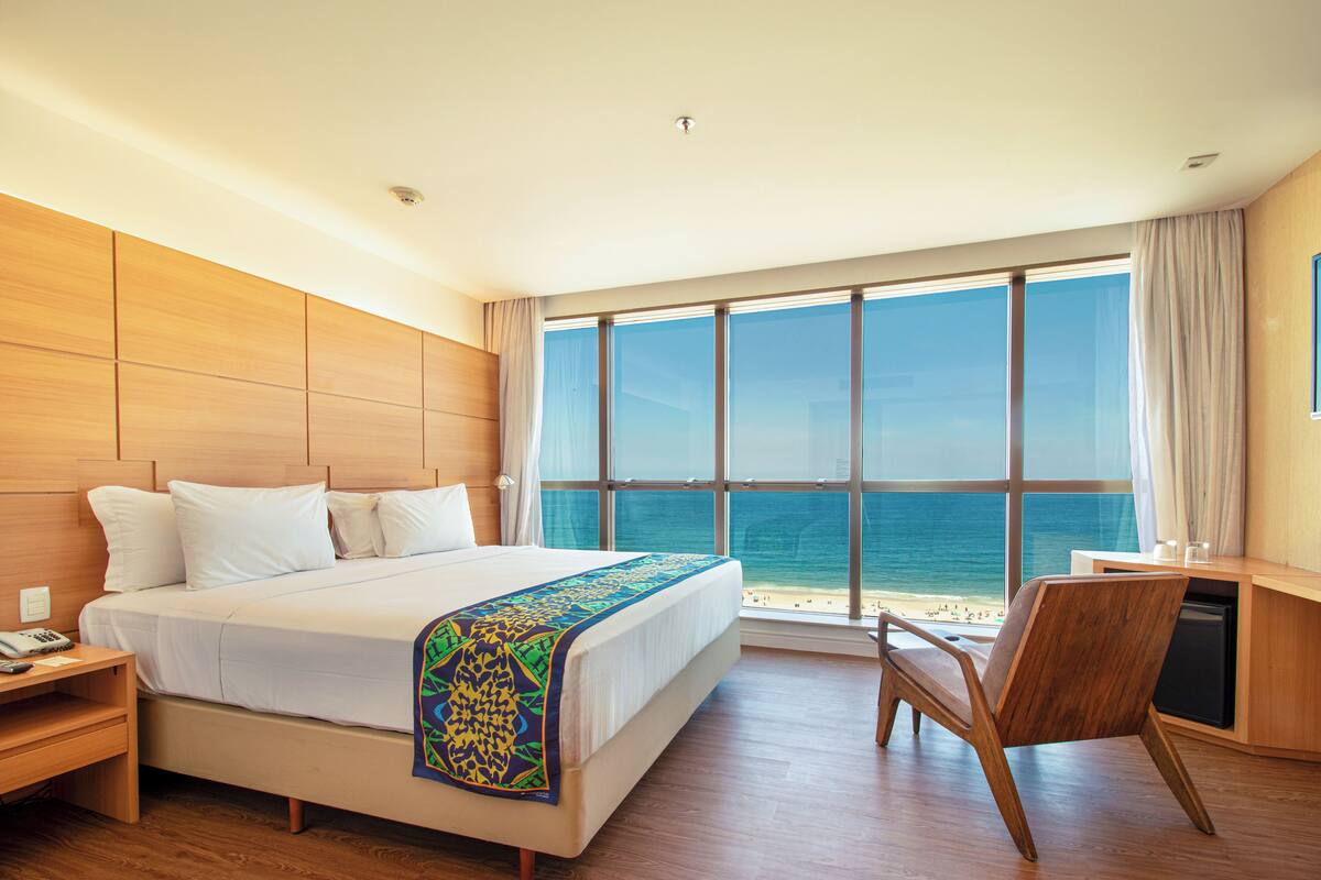 A hotel room with a large bed, a desk, and a view of the ocean.
