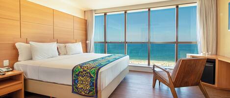 Een hotelkamer met een groot bed, een bureau en uitzicht op de oceaan.