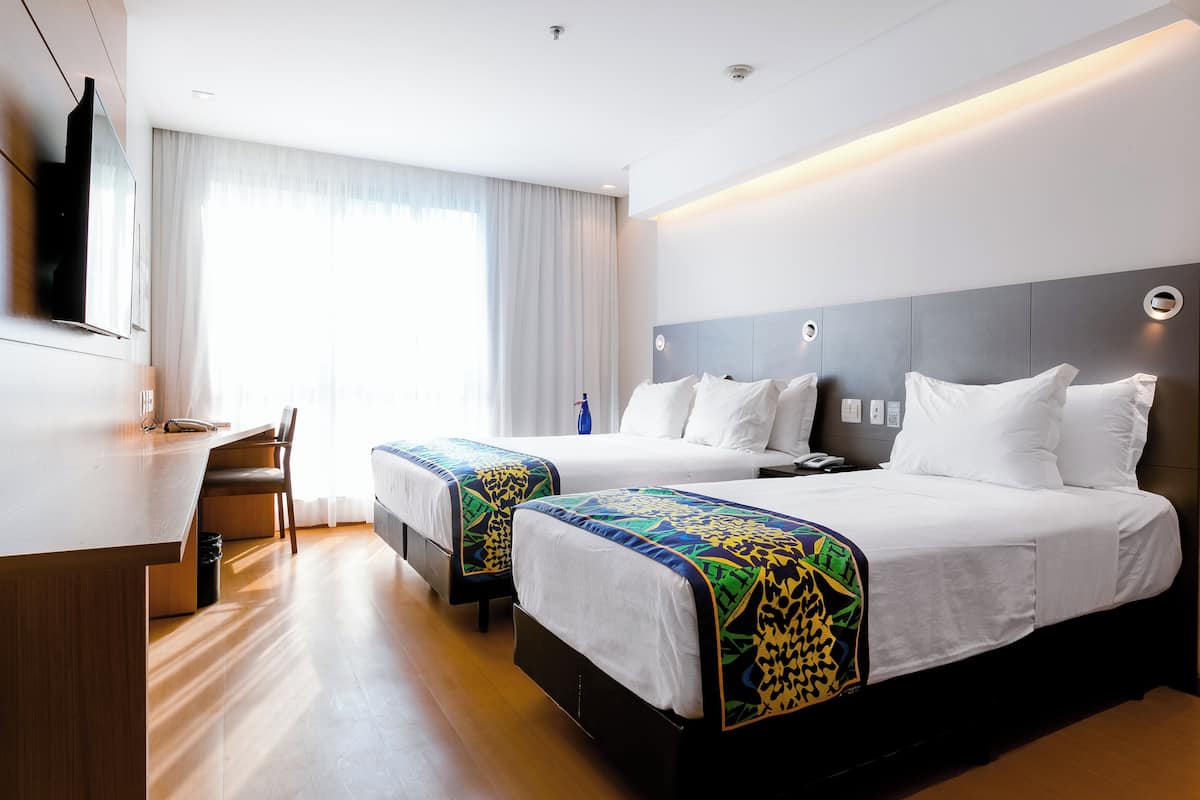 A hotel room with two beds, a desk, a chair, and a TV mounted on the wall.