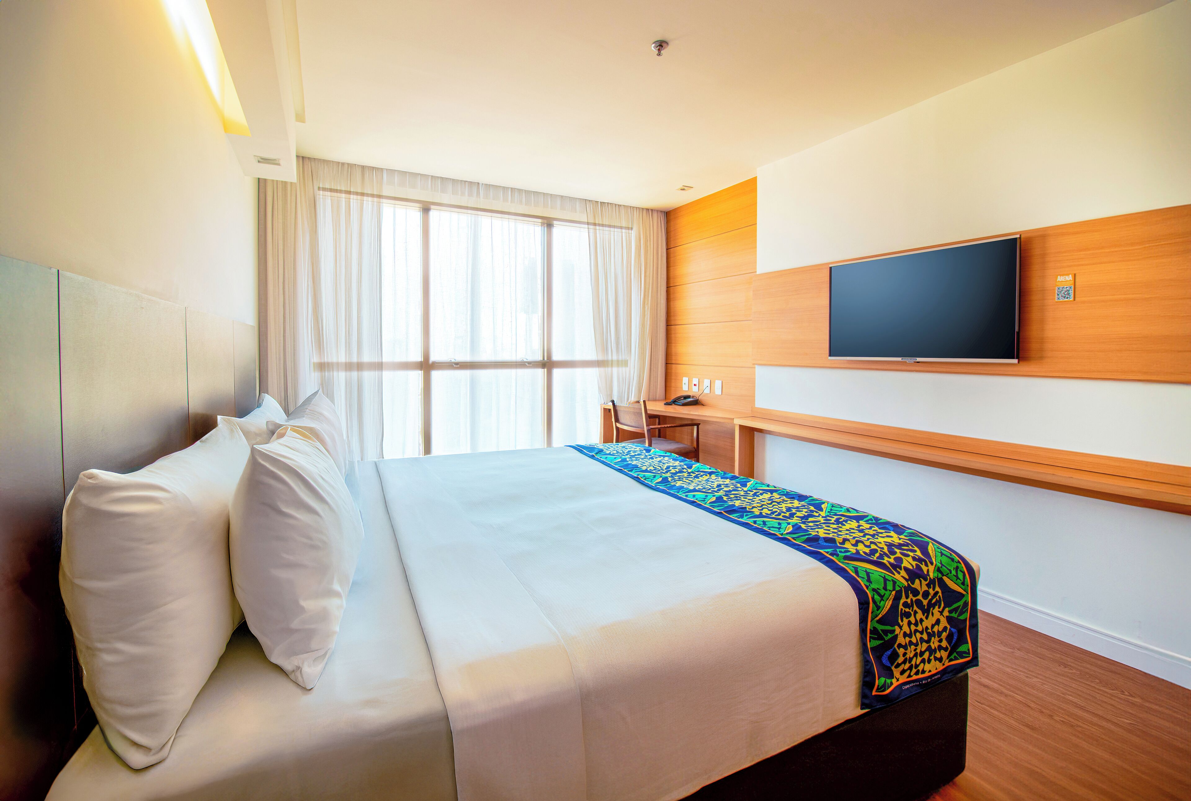 A hotel room with a bed, a desk, a chair, a television, and a window with curtains.