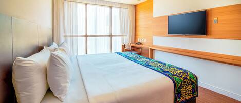 A hotel room with a bed, a desk, a chair, a television, and a window with curtains.