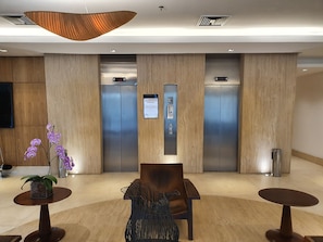 A modern lobby with two elevators, a reception desk, and a seating area with a vase of flowers.