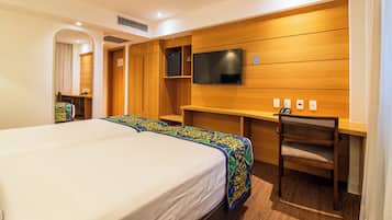 A hotel room with a large bed, a desk with a chair, a television, and a wardrobe.