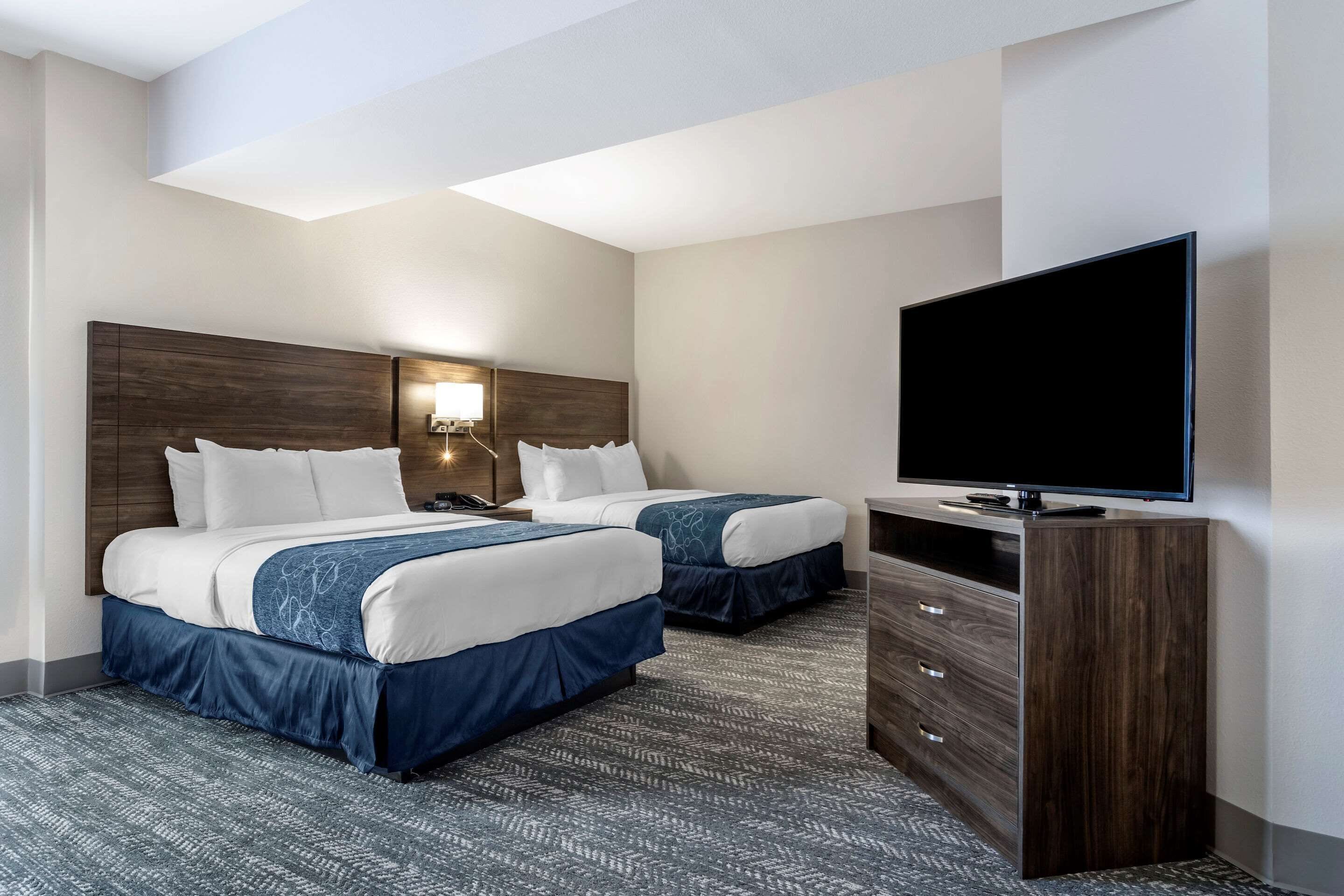 Une chambre d’hôtel avec deux lits, une télévision, une commode et une table de chevet avec une lampe.