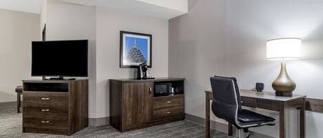 A hotel room with a flat-screen TV, a wooden cabinet, a desk with a chair, and a lamp.
