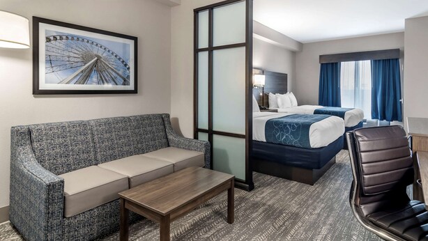 Une chambre d’hôtel avec un canapé, un lit, un bureau et une grande fenêtre avec des rideaux.