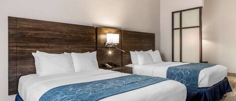 Quarto de hotel com duas camas, cabeceira de madeira, mesa de cabeceira com abajur e janela com persianas.