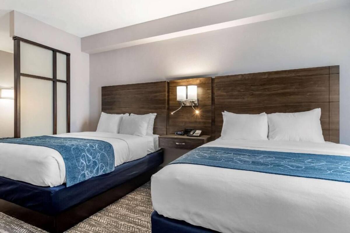 Een hotelkamer met twee bedden, een nachtkastje met een telefoon, en een wandlamp.