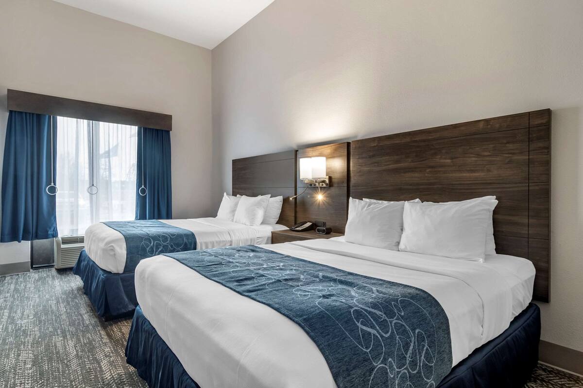 Een hotelkamer met twee bedden, een groot raam met gordijnen, een wandlamp en een telefoon op het nachtkastje.