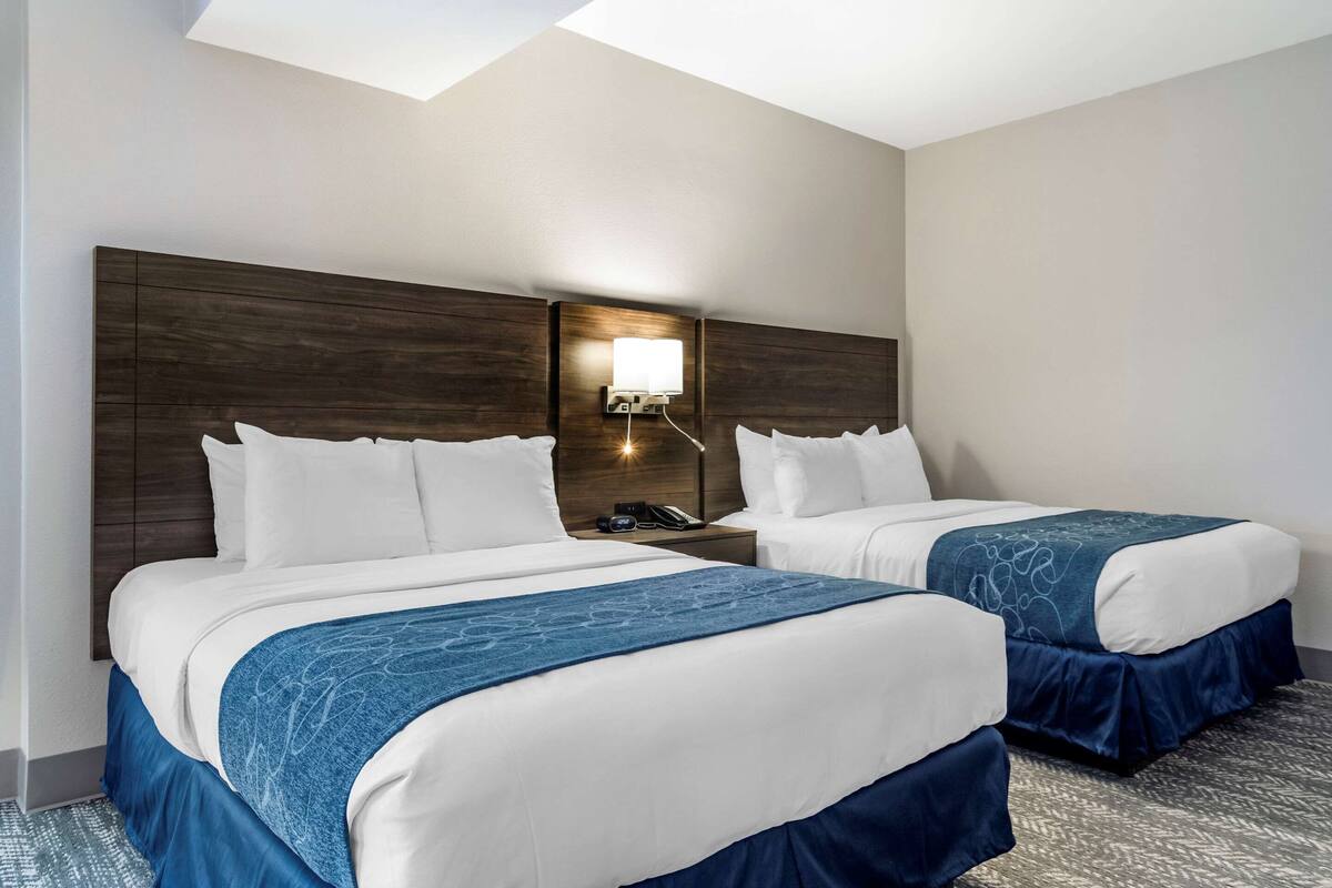 Een hotelkamer met twee bedden, een nachtkastje met een lamp en een groot raam.