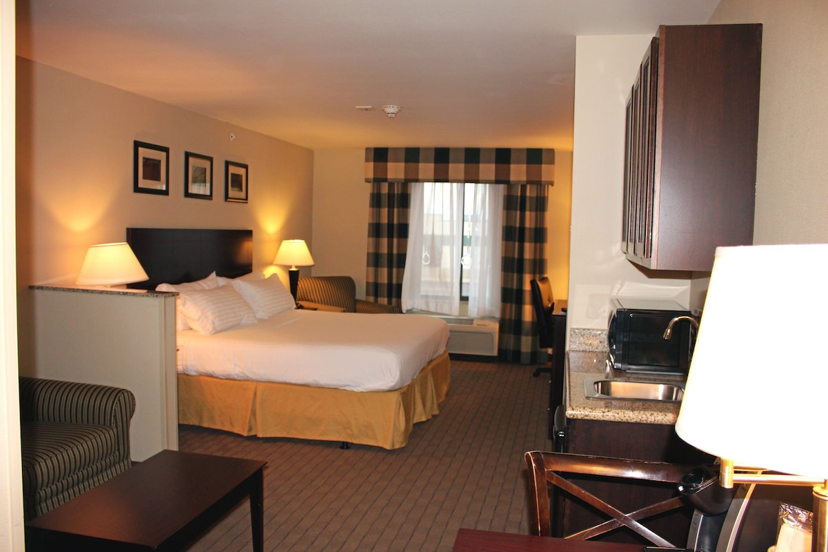 A hotel room with a bed, a desk, a chair, a TV, and a kitchenette.