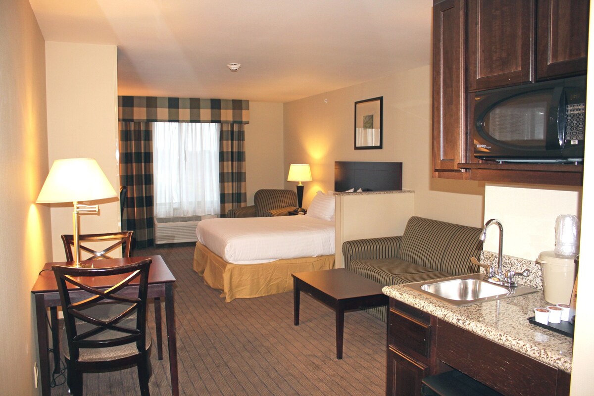 A hotel room with a bed, a sofa, a desk, a lamp, a microwave, and a sink.