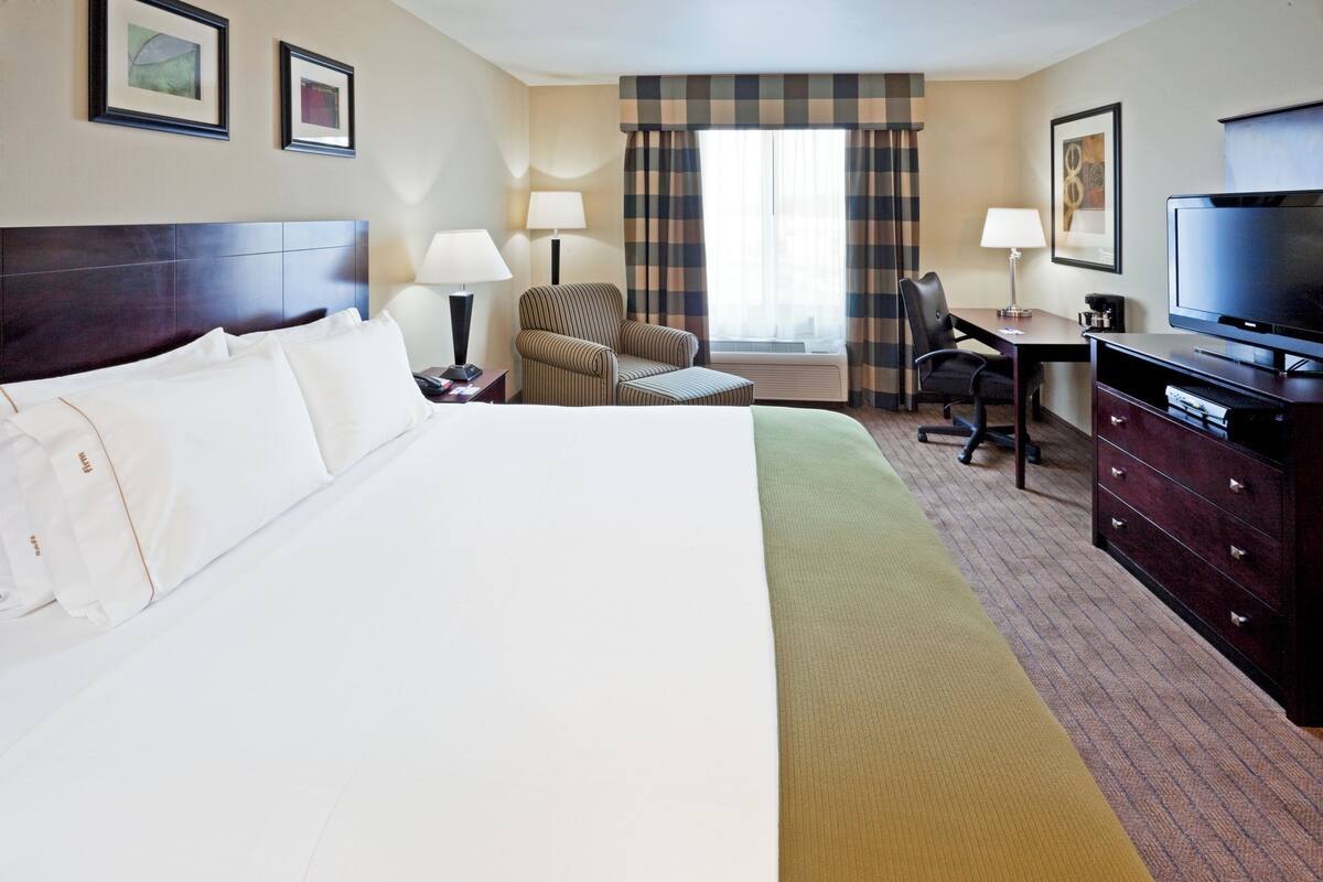 A hotel room with a large bed, a desk, a chair, a television, and a window with curtains.