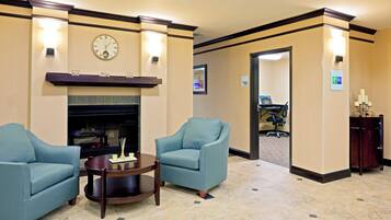 A lobby with two armchairs, a small table, a fireplace, and a clock on the wall.