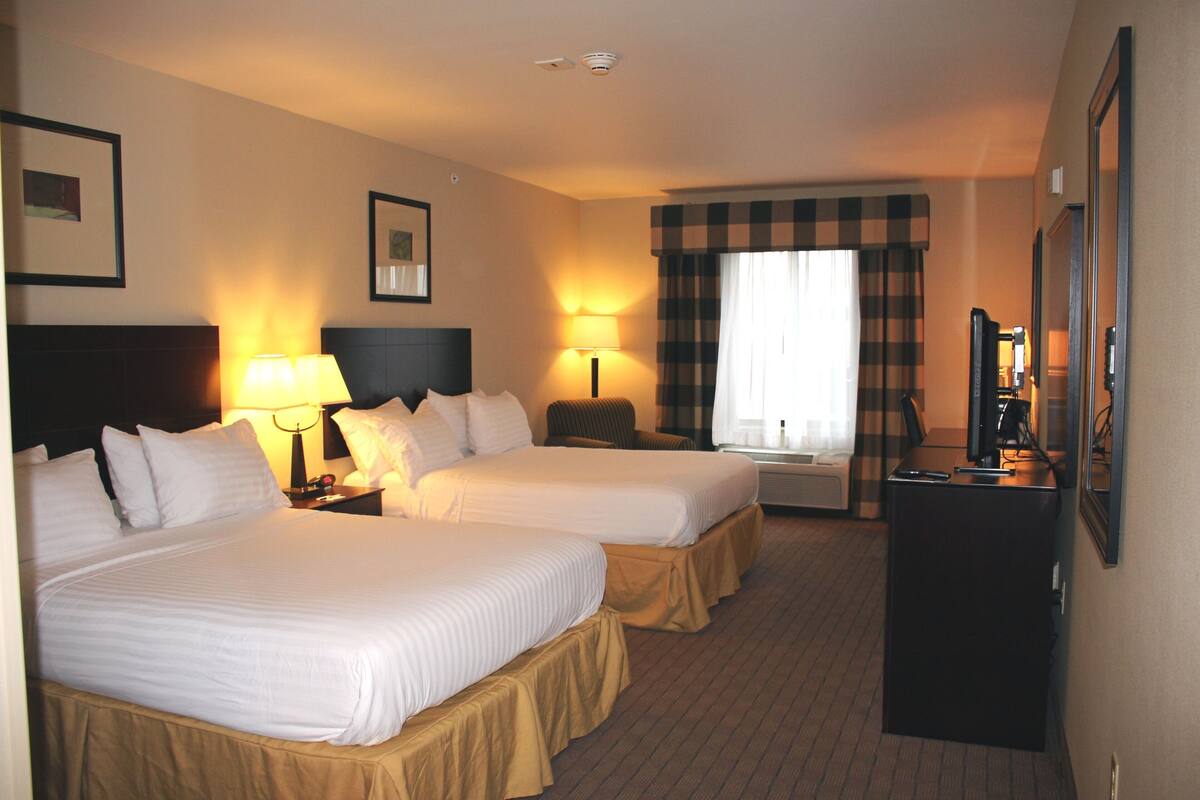 A hotel room with two beds, bedside lamps, a desk with a computer, and a television.