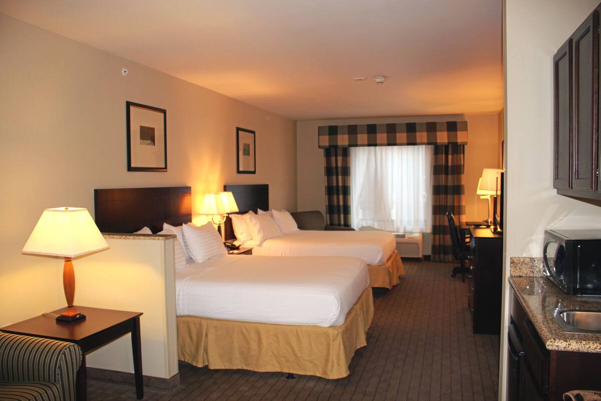 Een hotelkamer met twee bedden, een bureau, een stoel, een magnetron en een raam met gordijnen.