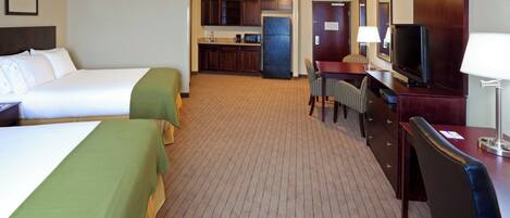 A hotel room with two beds, a kitchenette, a desk with a TV, and a chair.