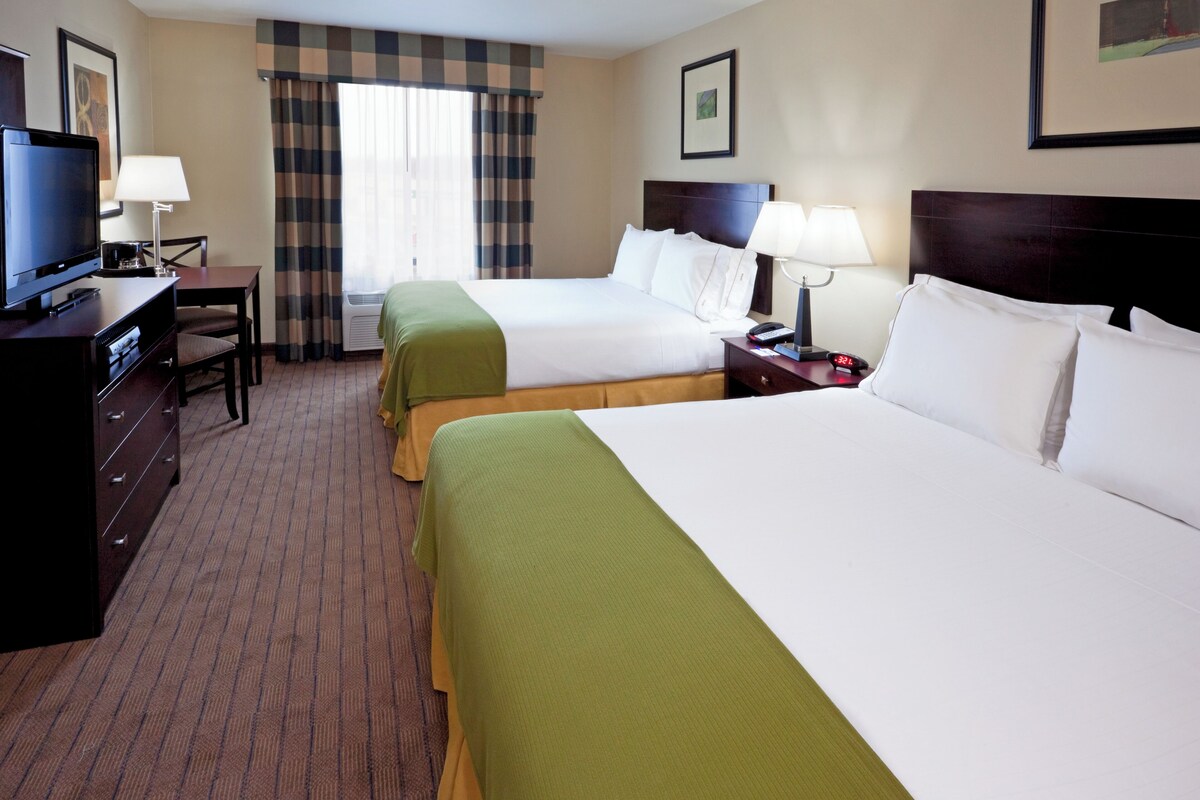 A hotel room with two beds, a desk with a television, and a window with curtains.