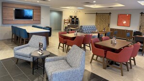 Un espace repas moderne avec plusieurs tables et chaises, un téléviseur à écran plat fixé au mur et un mur d’accent en bois.