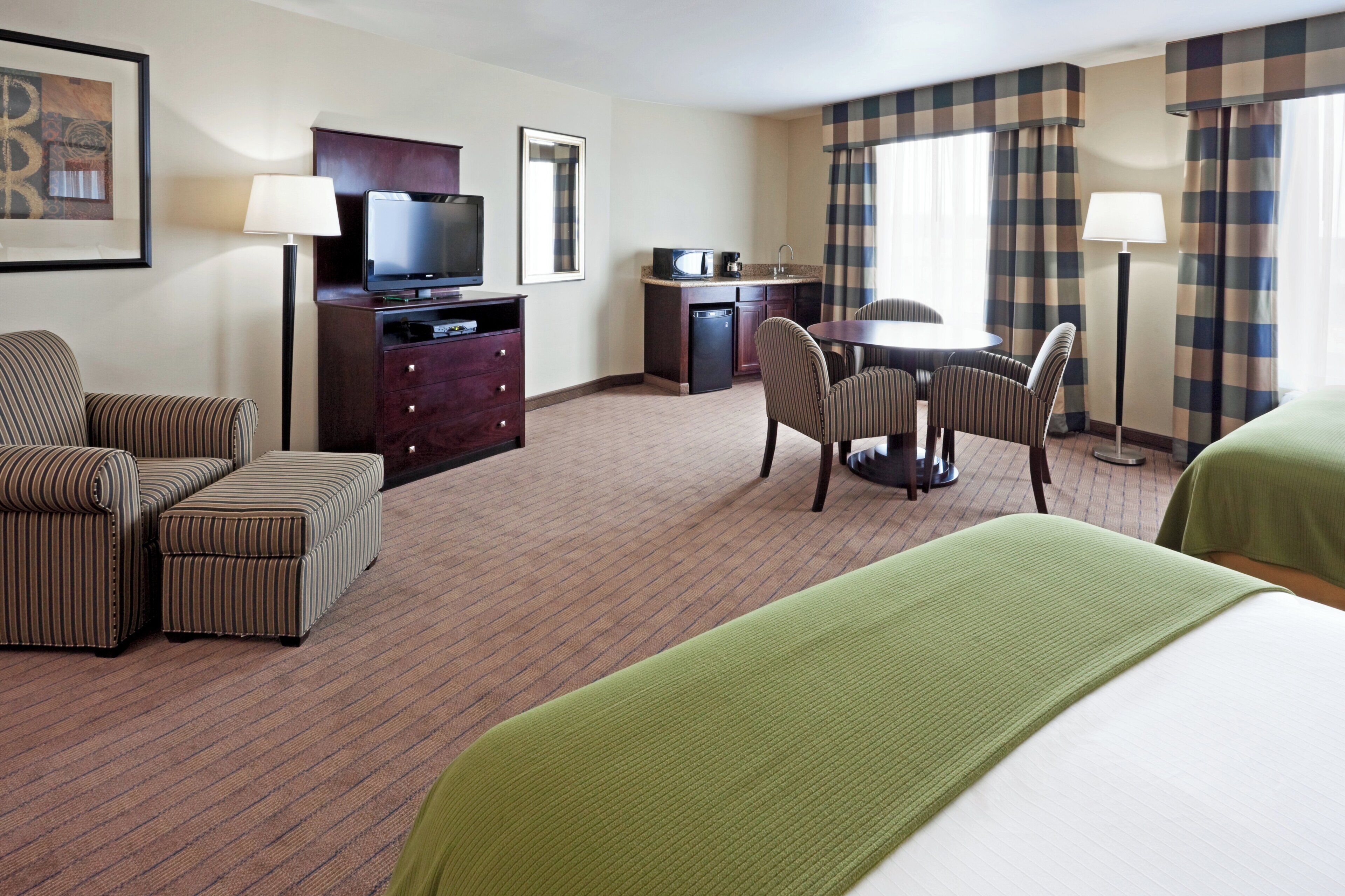 Una habitación de hotel con cama, escritorio con televisor, mesa de comedor con sillas y baño.