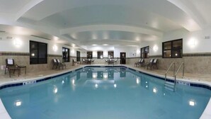 An indoor swimming pool with multiple lanes, surrounded by lounge chairs and a tiled wall.