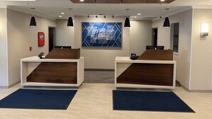 A reception area with two wooden reception desks, a blue geometric wall art, and a fire alarm on the left.