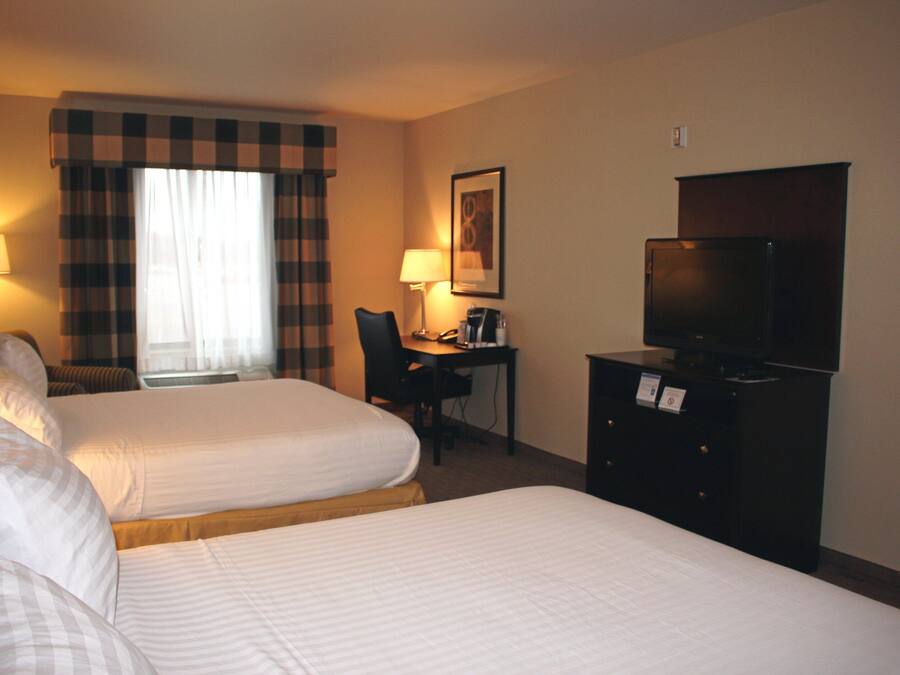 A hotel room with two beds, a desk with a chair, a television, and a lamp.