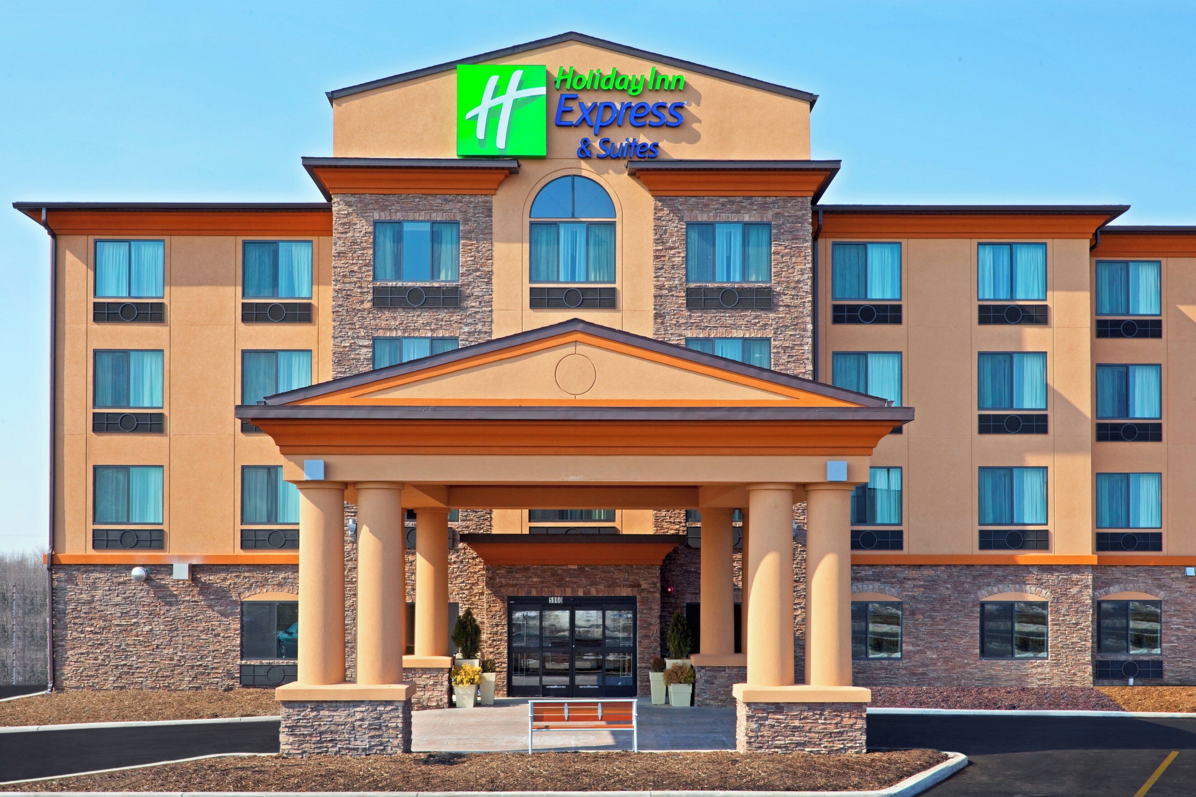 Un bâtiment de la chaîne Holiday Inn Express & Suites, doté d’une entrée imposante, de nombreuses fenêtres et d’une façade en pierre.